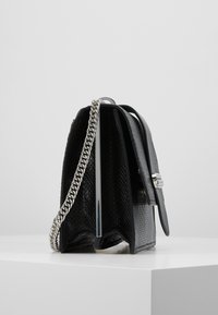 Borsa nera con texture, dotata di un manico a catena argentata, con chiusura a pattina e un design strutturato. Evidente per i suoi materiali a contrasto.