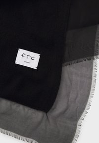 Sciarpa nera in cashmere con una superficie morbida e testurizzata. Presenta uno strato trasparente grigio e un'etichetta bianca con la scritta "FTC" e "CASHMERE" stampata.