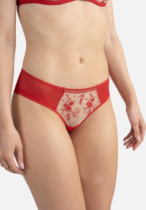 Mujer con ropa interior de encaje roja con bordado floral en panel de tela transparente en la parte frontal, mostrada desde la cintura hasta la mitad del muslo.