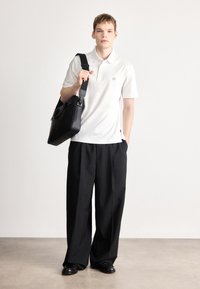 Μαύρη δερμάτινη τσάντα ταχυδρόμου, λευκό μπλουζάκι πόλο και άνετο μαύρο παντελόνι. Το μπλουζάκι πόλο έχει μικρό λογότυπο. Απλός, μοντέρνος σχεδιασμός.