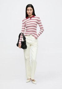 Rood-wit gestreept geribd topje met lange mouwen en een rode kraag, gecombineerd met crème-kleurige broek met rechte pijpen en een zwarte handtas.