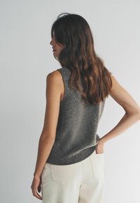 Bezrukávový sivý pletený top s textúrovaným povrchom, doplnený svetlo béžovými nohavicami s vysokým pásom. Zadný pohľad zobrazuje detaily ramien a chrbta.