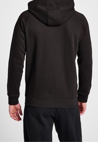 Svart huvtröja med en slät textur, raglanärmar och ribbade muddar. Baksidan har minimala sömmar och en klassisk design.