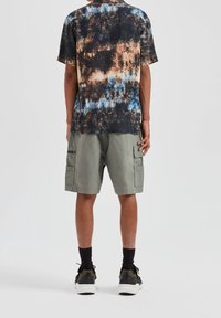 Kurzärmliges T-Shirt mit Batikmuster in Schwarz-, Blau- und Brauntönen, kombiniert mit olivgrünen Cargo-Shorts mit Seitentaschen und einer entspannten Passform.