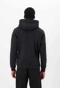 Haut à capuche noir en tissu doux, doté d'une grande capuche et de poignets côtelés, associé à un jean sombre pour un look décontracté.