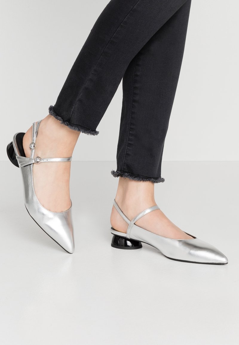Chaussures slingback métalliques argentées à bout pointu, avec des fines brides et un petit talon noir. Texture lisse avec peu de détails.