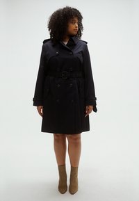 Tengerészkék ballonkabát dupla soros gombokkal, öves derékkal, vállpántokkal és középhosszú szabással. Simább anyag és klasszikus dizájn.