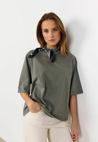 Oliven grøn kortærmet T-shirt med løs pasform og rund hals. Parret med et mønstret sort-hvidt tørklæde om halsen.
