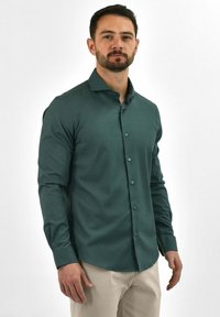 Groen overhemd met lange mouwen van gladde stof, met een knoopsluiting aan de voorkant, een getailleerde pasvorm en een klassieke kraag. Eenvoudig ontwerp zonder patronen.