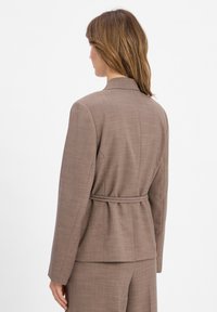 Blazer marron ajusté avec un design structuré, un tissu texturé et une taille ceinturée. Comprend une fente au dos et des manches longues.