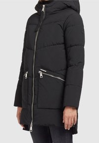 Doudoune noire avec capuche, dotée de fermetures éclair argentées, d'un motif matelassé et de poches zippées. Le matériau semble doux et isolé.