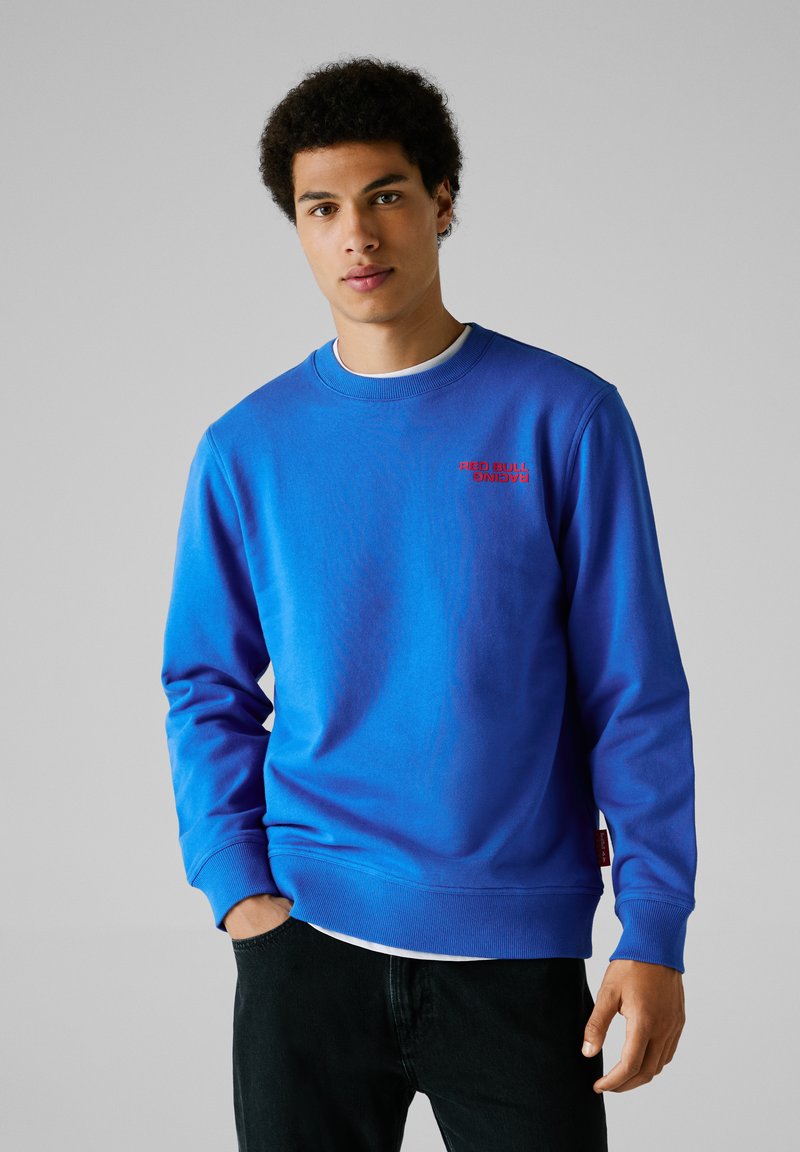 Blauw sweatshirt met ronde hals, gemaakt van zachte stof, met een rood "Red Bull Racing"-logo op de borst en geribbelde manchetten en zoom.