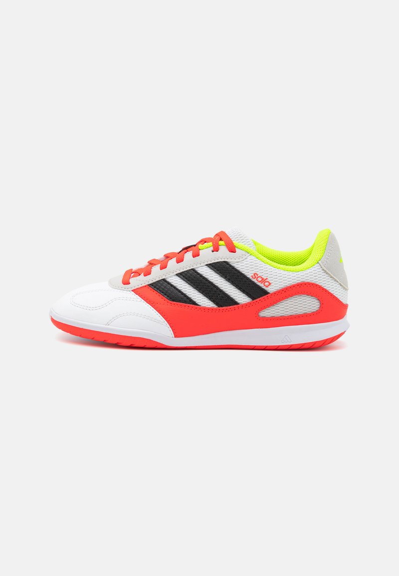Chaussure de sport blanche avec des accents gris, trois bandes noires, semelle rouge vif et détails en mesh jaune dans la zone du col.