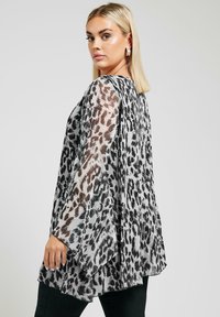 Genomskinlig, lätt blus med ett svart och grått leopardmönster, med vida ärmar och en lös, flödande silhuett.