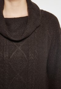 Donkerbruine trui met een kraag, geribbelde textuur en ruitpatronen op het lichaam, die de warmte en breidetailen benadrukt.