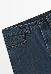 Jeans in denim blu scuro con una finitura leggermente sbiadita. Presentano quattro tasche, rivetti in rame e chiusura con bottone. Tessuto testurizzato con cuciture tradizionali.