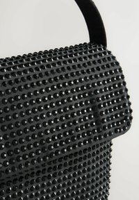 Black handbag with flap, fully covered in small black studs, and a short black handle against a plain light background.