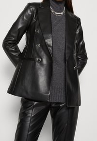 Blazer en cuir noir croisé avec boutons métalliques, doté d'une silhouette ajustée, de poches latérales et de détails de couture contrastants.