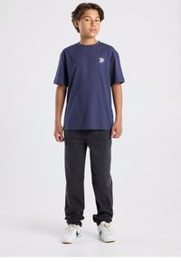 Navy blue cotton t-shirt with short sleeves, featuring a chest graphic and paired with black pants and white sneakers.