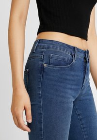 Vaqueros de mezclilla azul con un diseño ajustado, bolsillo frontal visible y cremallera. La tela parece ligeramente desgastada y tiene una textura suave.