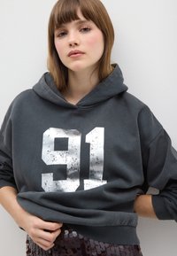 Felpa grigia con cappuccio, caratterizzata da una grande stampa argentata "91" usurata sul davanti. Tessuto morbido con vestibilità comoda e orlo a costine.
