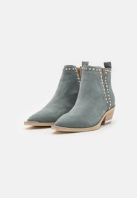 botas de ante hasta el tobillo en un azul verdoso apagado con punta afilada, tacones pequeños y detalles de tachuelas plateadas a lo largo de los costados.