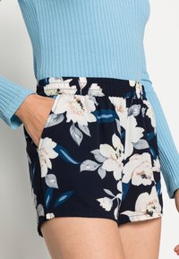 Szorty w granatowym kolorze z nadrukiem kwiatowym w odcieniach bieli i niebieskiego. Elastyczny pas i boczne kieszenie. Lekki materiał o miękkiej fakturze.