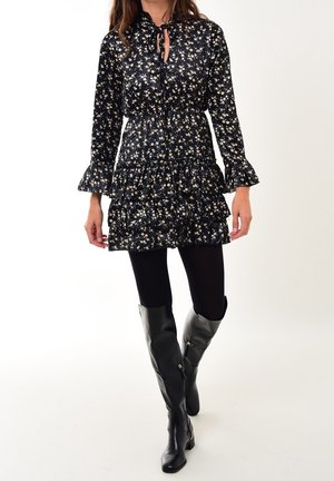 Vestido negro con flores, de mangas largas y con un dobladillo acampanado. Presenta un escote con lazo y se combina con botas altas negras brillantes.