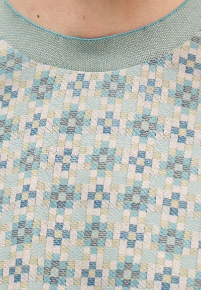 Κοντινό πλάνο πουλόβερ με πλεκτό μοτίβο και εικονοστοιχειώδη σχεδίαση σε αποχρώσεις του μπλε, μπεζ και ανοιχτό πράσινο γύρω από το λαιμό.