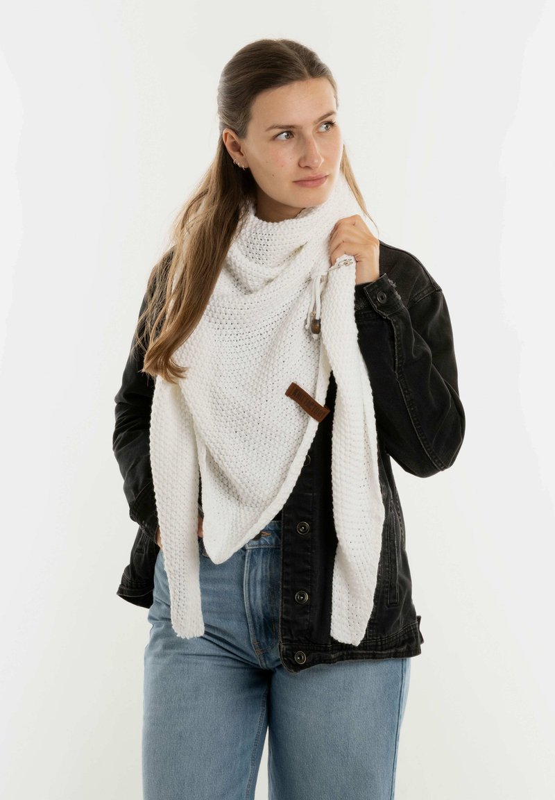 Witte gebreide sjaal met een textuurpatroon, om de nek gedrapeerd, met een houten accent en een verstelbare strik, in combinatie met een zwarte jas.