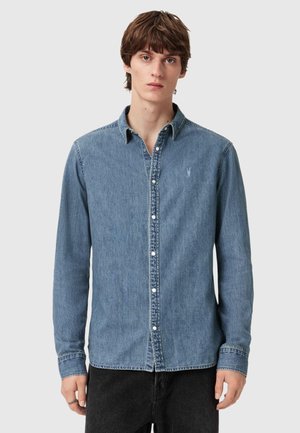 Chemise en denim à manches longues dans un délavé bleu clair, avec un col boutonné, des boutons à l'avant et un petit logo brodé sur la poitrine.