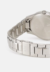 Hõbedane roostevabast terasest kell linkkettiga, millel on ruudukujulised lingid ja poleeritud pind. Omab sujuvat ümarat tagakapse.