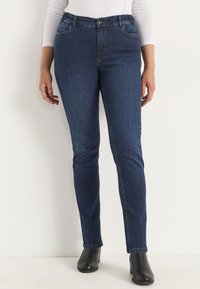 Höga jeans i mörkblå denim med en slät yta, försedda med framfickor och knappstängning, som kompletterar svarta ankelstövlar.