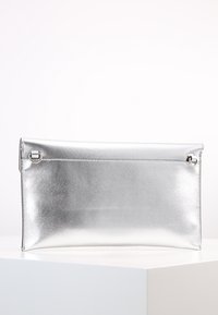 Metaliczna srebrna kopertówka o gładkiej fakturze, prostokątnym kształcie i detalach w postaci zamków po bokach. Prosty design z czystym wykończeniem.