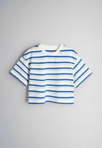 Chemise blanche à manches courtes et courte avec des rayures horizontales bleues, accrochée sur un fond gris clair uni.