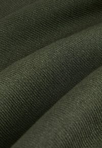 Donkergroene, gestructureerde stof met een nauwkeurig geweven structuur, waardoor zichtbare vezels en een zachte, duurzame oppervlakte zichtbaar zijn.