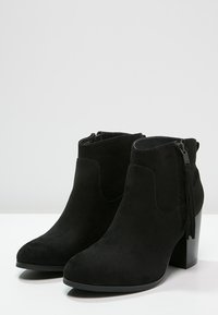 Czarne zamszowe botki za kostkę z okrągłym noskiem, z boku zapinane na zamek błyskawiczny oraz z teksturowanym detalem w postaci frędzla na zamku. Posiadają blokowy obcas.