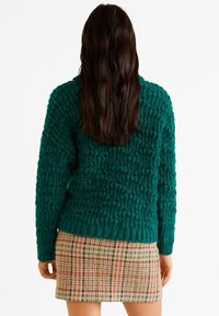Teksturowany niebieskozielony sweter o luźnym kroju, połączony z mini spódnicą w kratę z czerwonymi, żółtymi i zielonymi akcentami. Przytulny, dzianinowy wygląd.