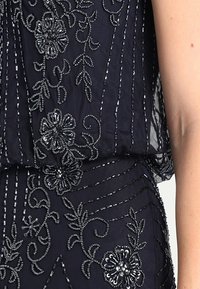 Námořnická látka s jemným květinovým výšiváním a flitry. Lehčí překrytí vytváří vrstvenou texturu, která zdůrazňuje elegantnost oděvu.