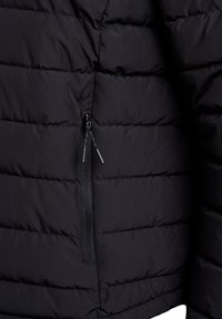Nahaufnahme einer schwarzen, gesteppten Jacke mit horizontalen Nähten und einer vertikalen, mit einem Reißverschluss versehenen Tasche mit zwei schwarzen Zugbändern auf der Vorderseite.
