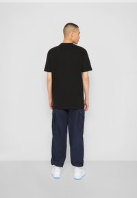 Schwarzes kurzärmeliges T-Shirt kombiniert mit navyfarbigen Cargo-Hosen und weißen Sneakern. Der Stoff wirkt glatt; das Shirt hat einen klassischen Rundhalsausschnitt.