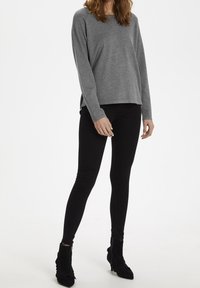 Maglietta grigia a maniche lunghe abbinata a jeans skinny neri, con un design elegante e stivaletti neri con accento in tessuto testurizzato.