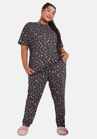 Pijama gris con un patrón de estrellas en rosa, naranja y blanco. Camiseta de manga corta y pantalones con cinturilla elástica, acompañados de zapatillas de casa rosas y esponjosas.