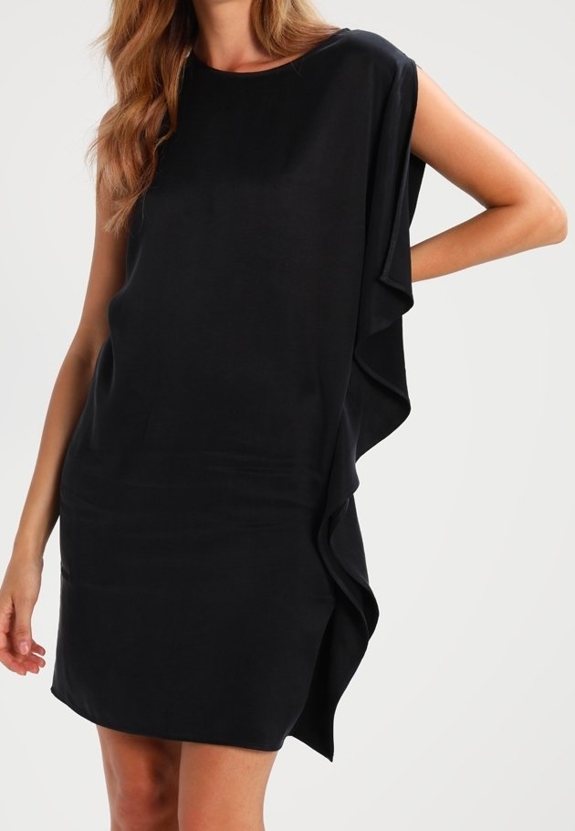 Robe noire ample avec des manches courtes, présentant un design drapé et une texture douce. L'ourlet est asymétrique avec un léger volant sur le côté.