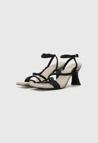 Schwarze Absatzsandalen mit einem einzigartigen gewundenen Riemendesign, ausgestattet mit einer beigen Innensohle und einem gebogenen Absatz, geeignet für formelle Anlässe.
