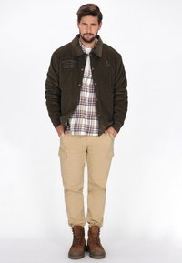 Sötétzöld kordbársony dzseki, gallérral, párosítva kockás inggel, bézs cargo nadrággal és barna csizmával. Texturált anyag és látható varrás.