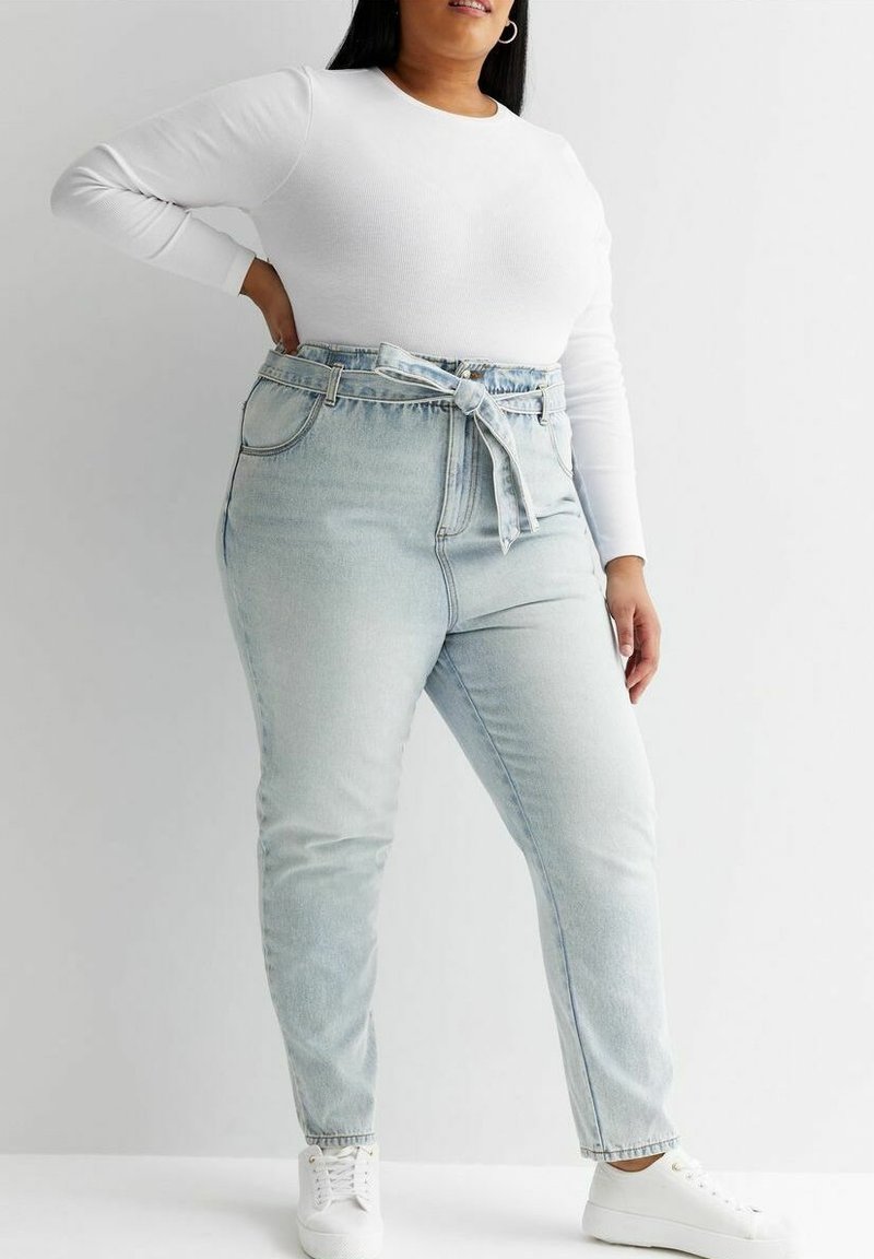 Top blanco de manga larga combinado con jeans de mezclilla de tiro alto en un tono azul claro. Los jeans cuentan con un cinturón atado y un corte recto, con una textura suave.