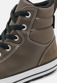 Sneakers înalte din piele maro și pânză, cu șireturi negre, ochiuri din metal argintiu, cusături albe și o talpă din cauciuc texturat.