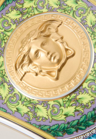 Prato de cerâmica com padrão intrincado de folhagem verde. Medaillon central dourado apresenta um design de face texturizada, com uma borda em motivo grego.