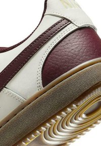 Zapatillas blancas y burdeos con parte superior de cuero texturizado, puntera redondeada, rayas laterales en contraste y suela de goma acanalada.